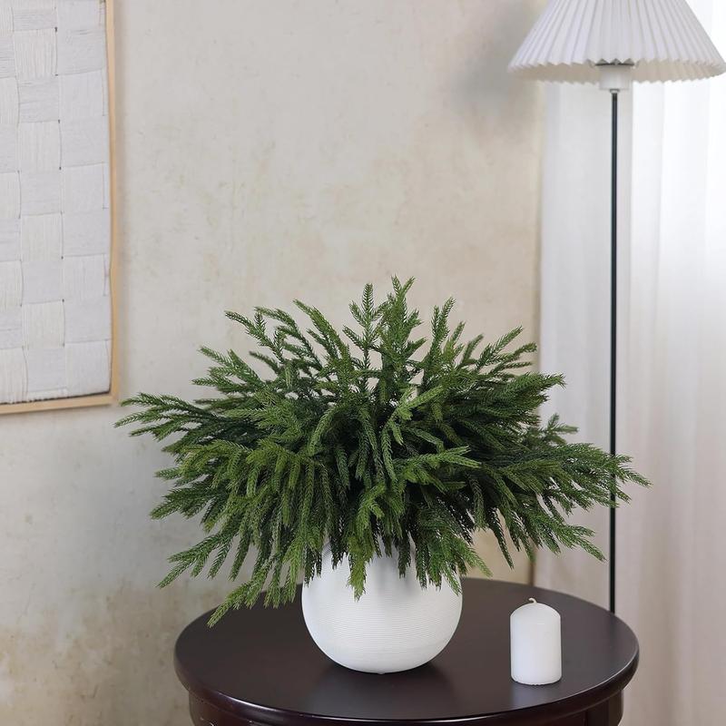 Artificial Norfolk pine branches in a white vase on a round side table