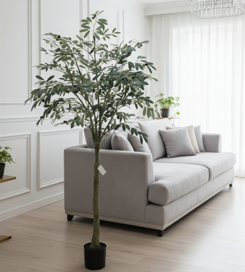Artificial olive tree with green leaves and faux olives in a black pot beside a gray sofa