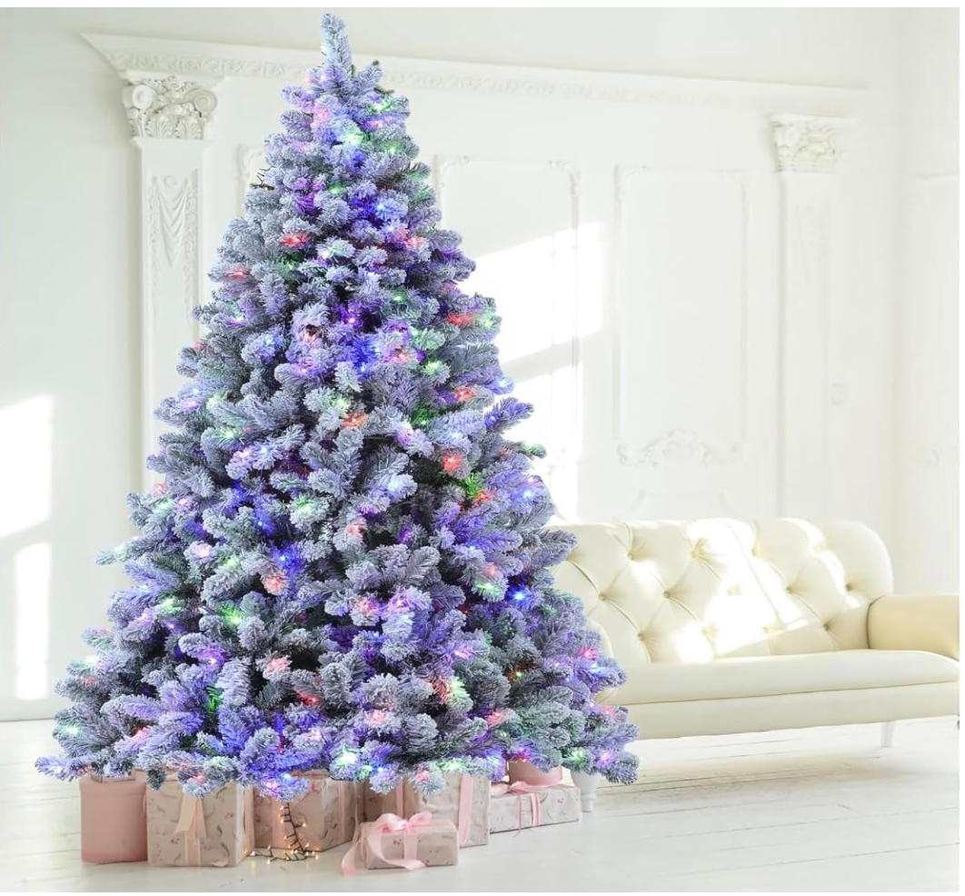 Silvanest snow-flocked Christmas tree with multicolor lights beside a white sofa in a bright living room